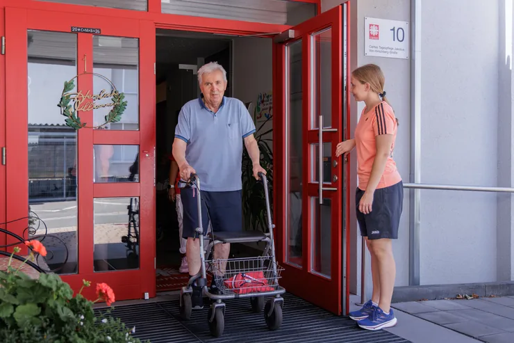 Physiotherapeutin holt einen Patienten mit Rollator an der Tür ab