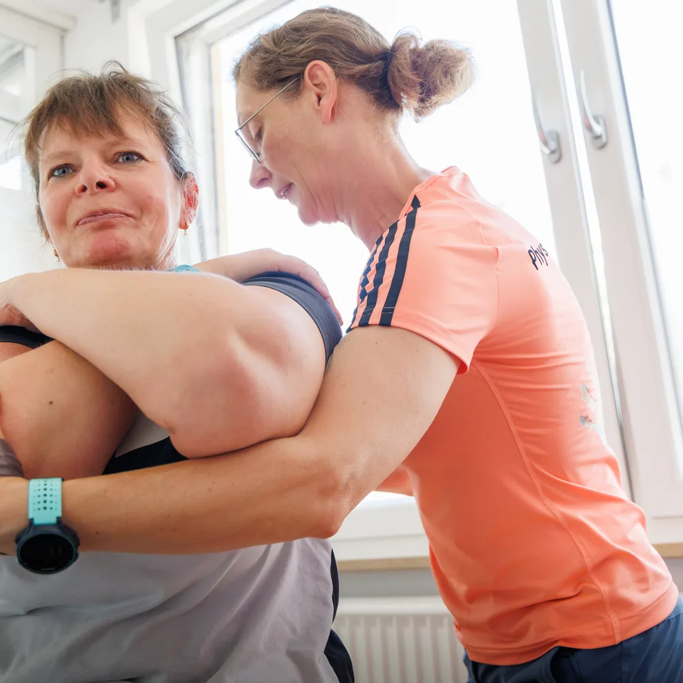 Physiotherapeutin mobilisiert die Schulter einer Patientin